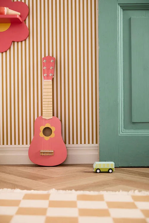 Kid's Concept wooden toy guitar against a striped wall with a green door and checkered floor