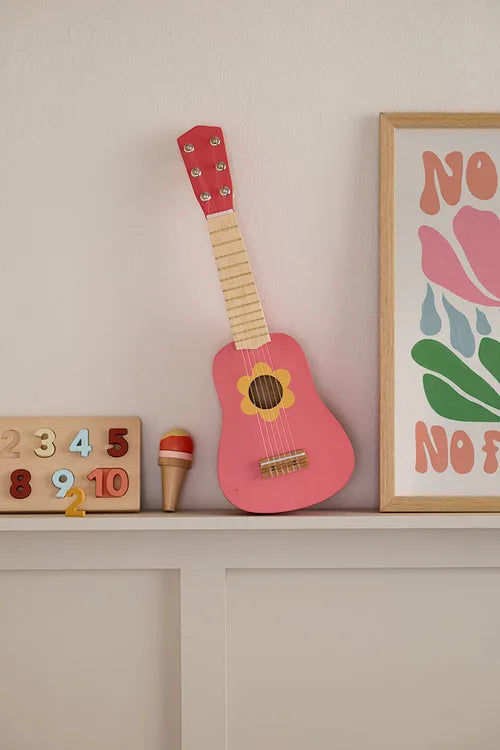 Kid's Concept wooden toy guitar on a shelf with a colorful poster and wooden toys (not included) in the background
