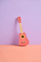 Kid's Concept wooden toy guitar on a peach surface with a purple background