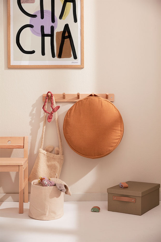 Kids Concept wall hook board with a round orange cushion, beige bag, and wooden chair against a light wall