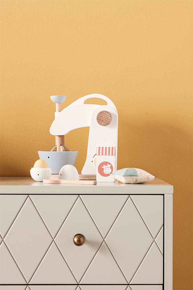 Kid's Concept wooden mixer set on a light gray cabinet with a yellow wall background