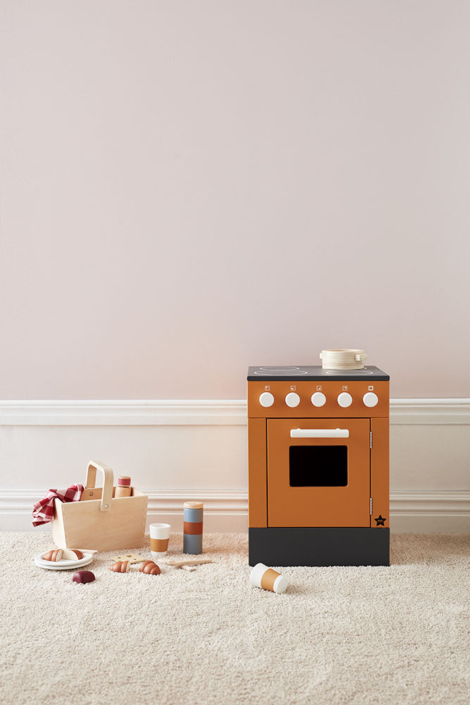 Kid's Concept picnic play set styled next to an orange kid's stove (not included) with black base on a light carpet against a neutral wall