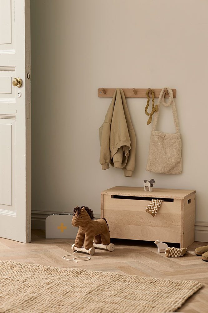 Wooden toy box with a Kid's Concept pull-along horse Vera, on a wooden floor in a room with a neutral color scheme