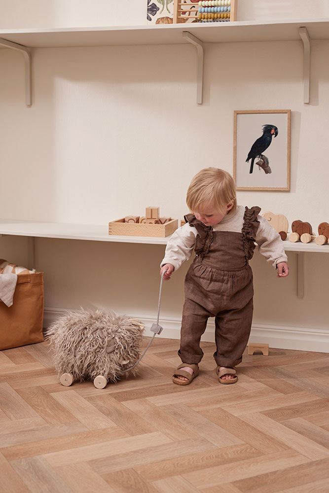 Child in brown overalls standing on a wooden floor playing with a Kid's Concept pull-along mammoth toy