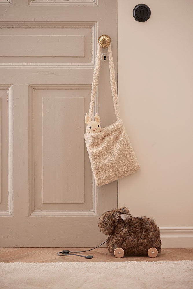 Beige plush bag with a small plush toy (not included) hanging on a door handle, next to a Kid's Concept pull-along moose toy