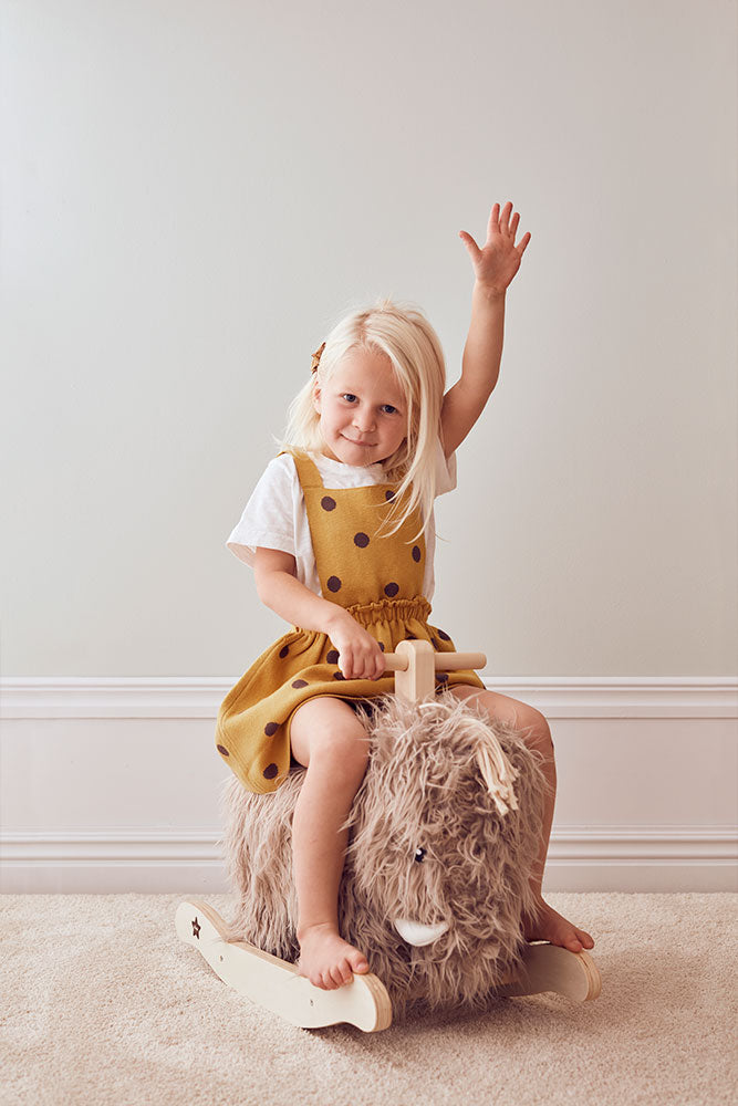 Child sitting on a Kid's Concept rocking horse Mammoth against a plain wall