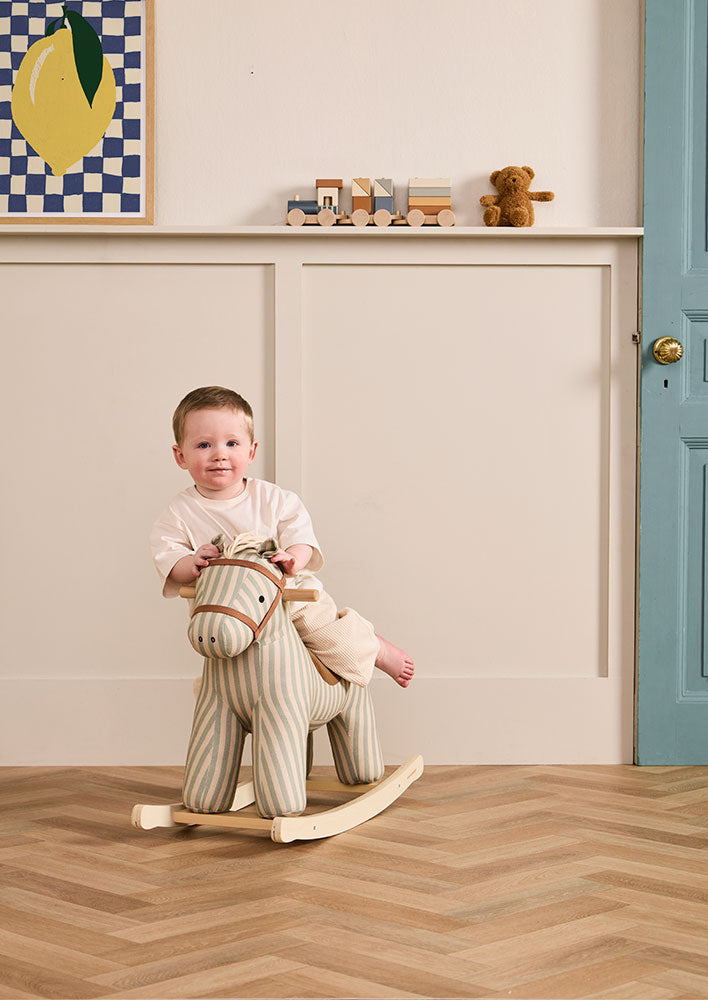 Child playing with a Kid's Concept rocking horse Sam in a room with toys on a shelf