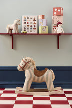 Kid's Concept rocking horse Sam on a checkered floor with shelves displaying toys and books in the background