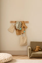 Decorative wall hook with a Kid's Concept snail dress-up costume, bags and a teddy bear on a beige wall
