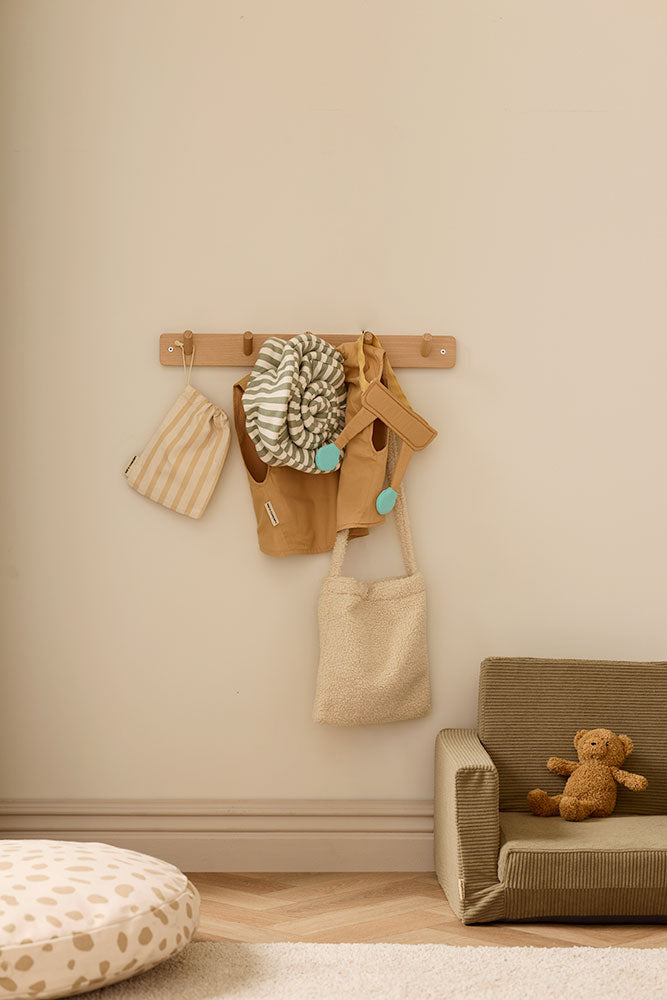 Decorative wall hook with a Kid's Concept snail dress-up costume, bags and a teddy bear on a beige wall