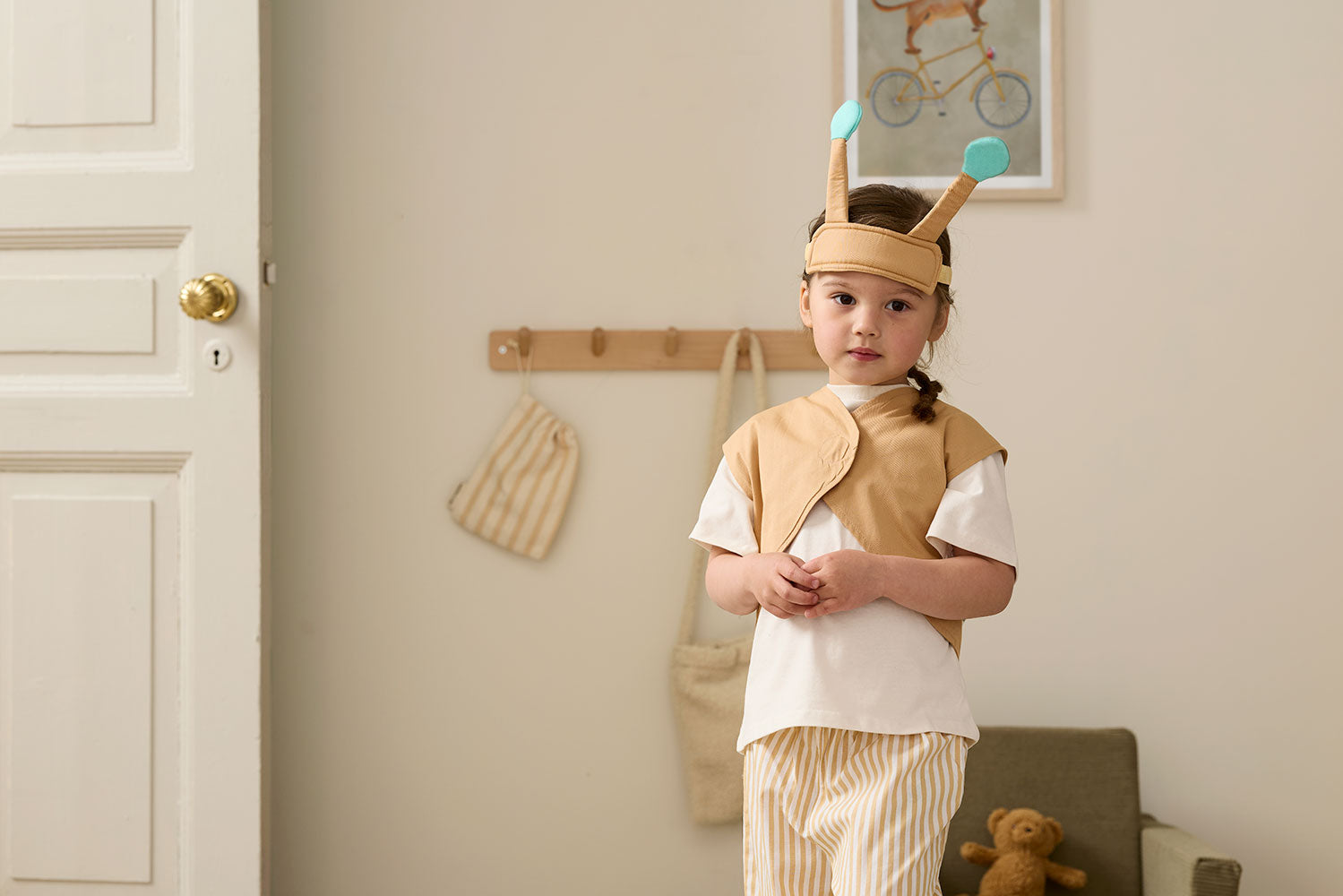 Child wearing a Kid's Concept snail dress-up costume in a room with a teddy bear (not included) and a door