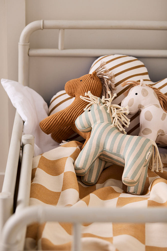 Kid's Concept soft toy horse Sam styled with different toy horses (not included) in a bed with checkered bedding