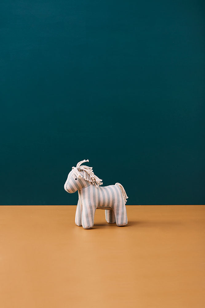 Kid's Concept soft toy horse Sam on a brown surface with a teal background