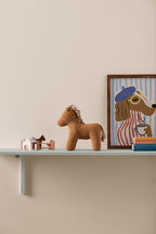 Shelf with a Kid's Concept soft toy horse Vera, framed picture of a dog, and books against a beige wall