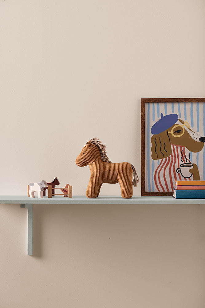 Shelf with a Kid's Concept soft toy horse Vera, framed picture of a dog, and books against a beige wall