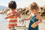 Two children by a body of water playing with a Kids Concept Swedish candy shop play set