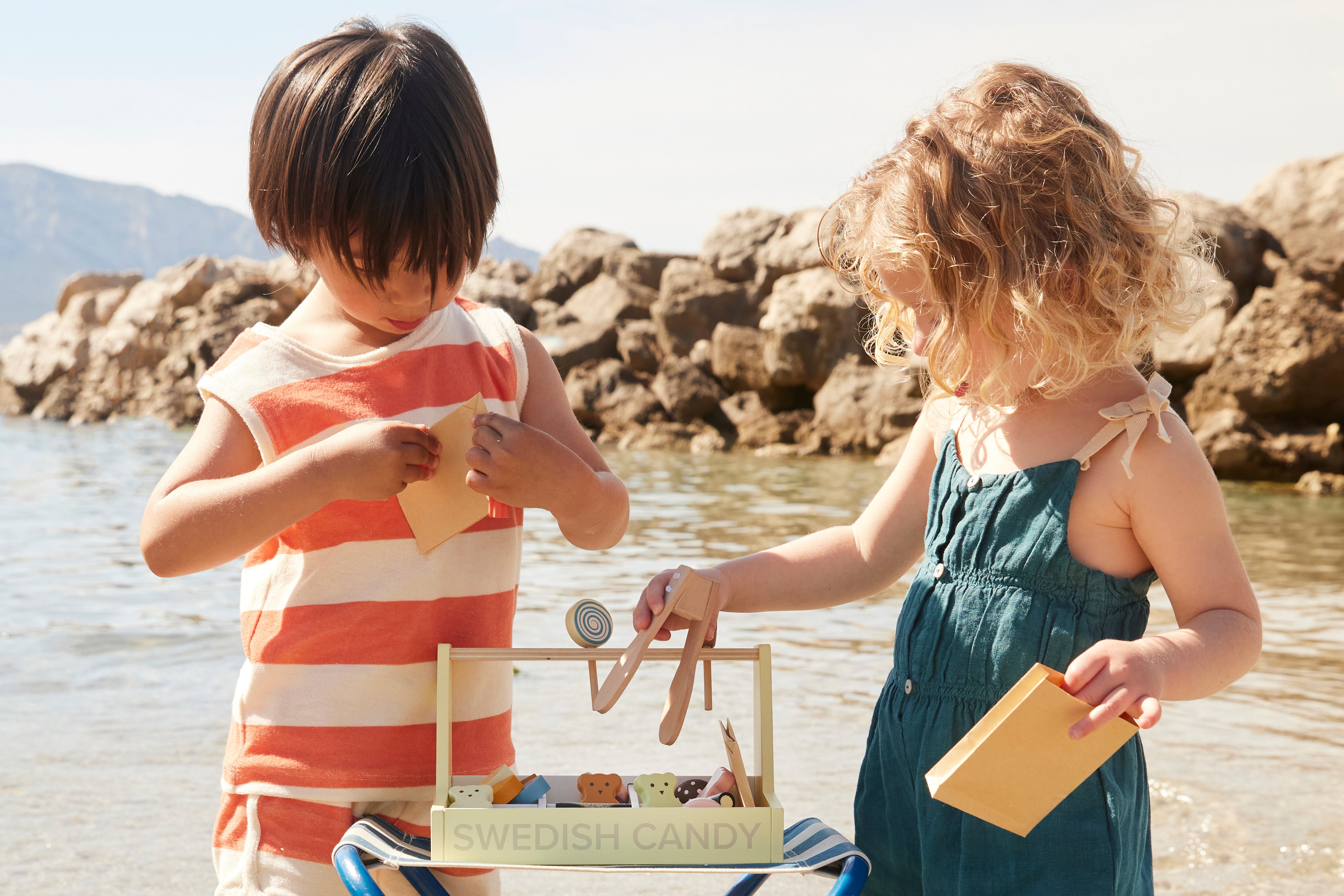 Two children by a body of water playing with a Kids Concept Swedish candy shop play set