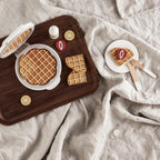 Kid's Concept wooden waffle iron toy on a wooden tray and light fabric background