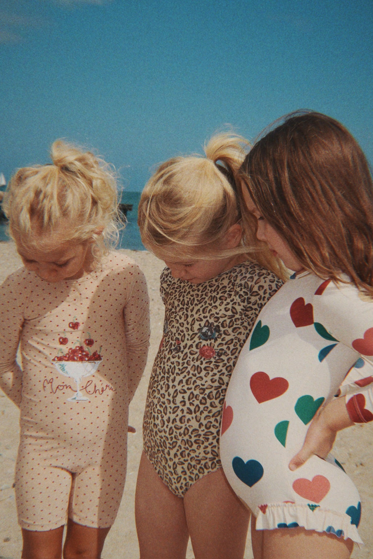 A child wearing the Konges Sløjd Amandine swim onesie in Emboldened not on a sandy beach, standing next to two other children