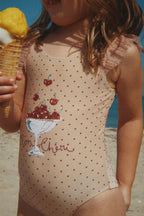 Close-up of a child in a Konges Sløjd Amandine swimsuit in Emboldened not, holding an ice cream cone on a beach.