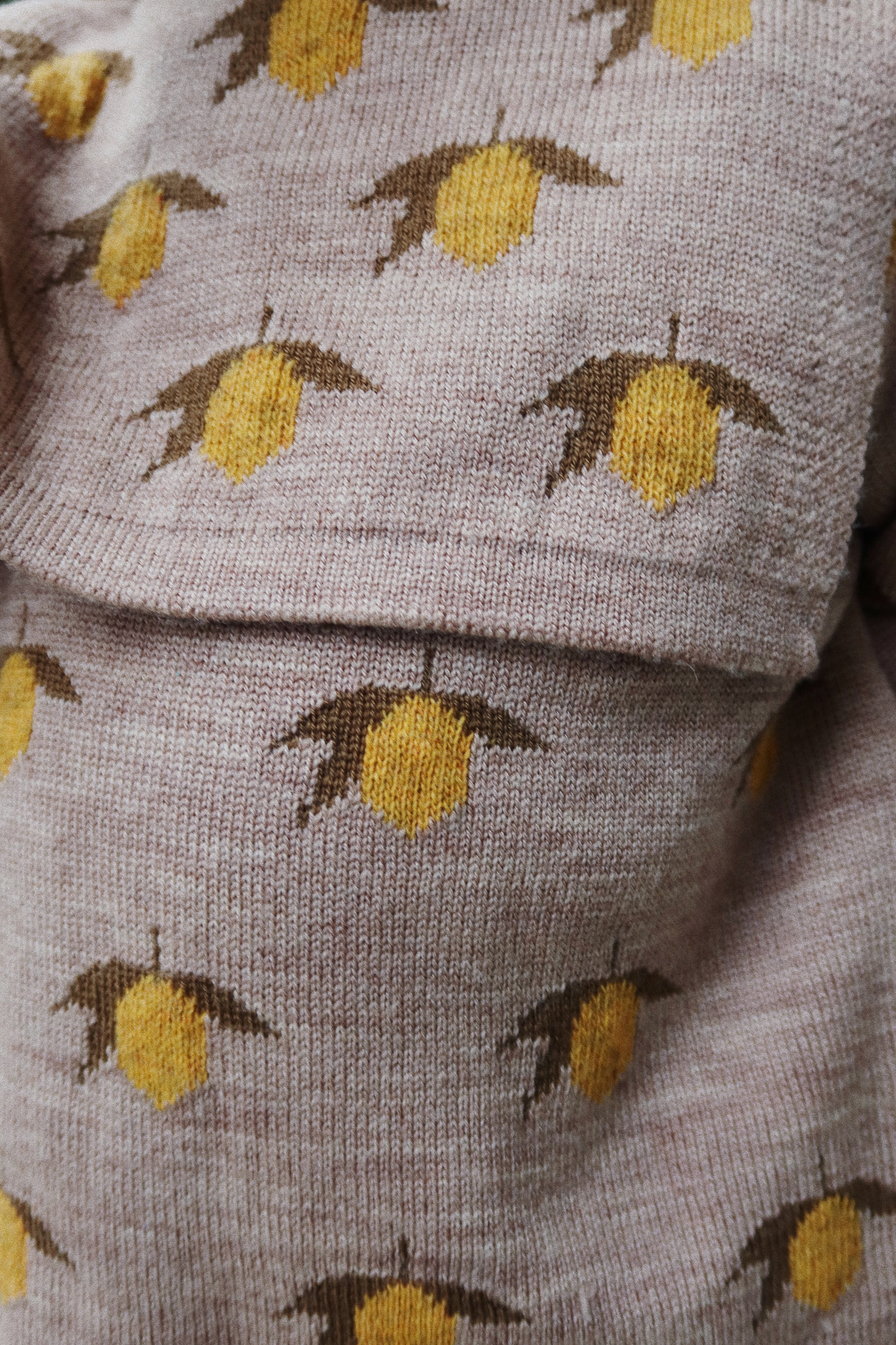 Close-up of Konges Sløjd Belou lemon knit sweater fabric and collar on white background