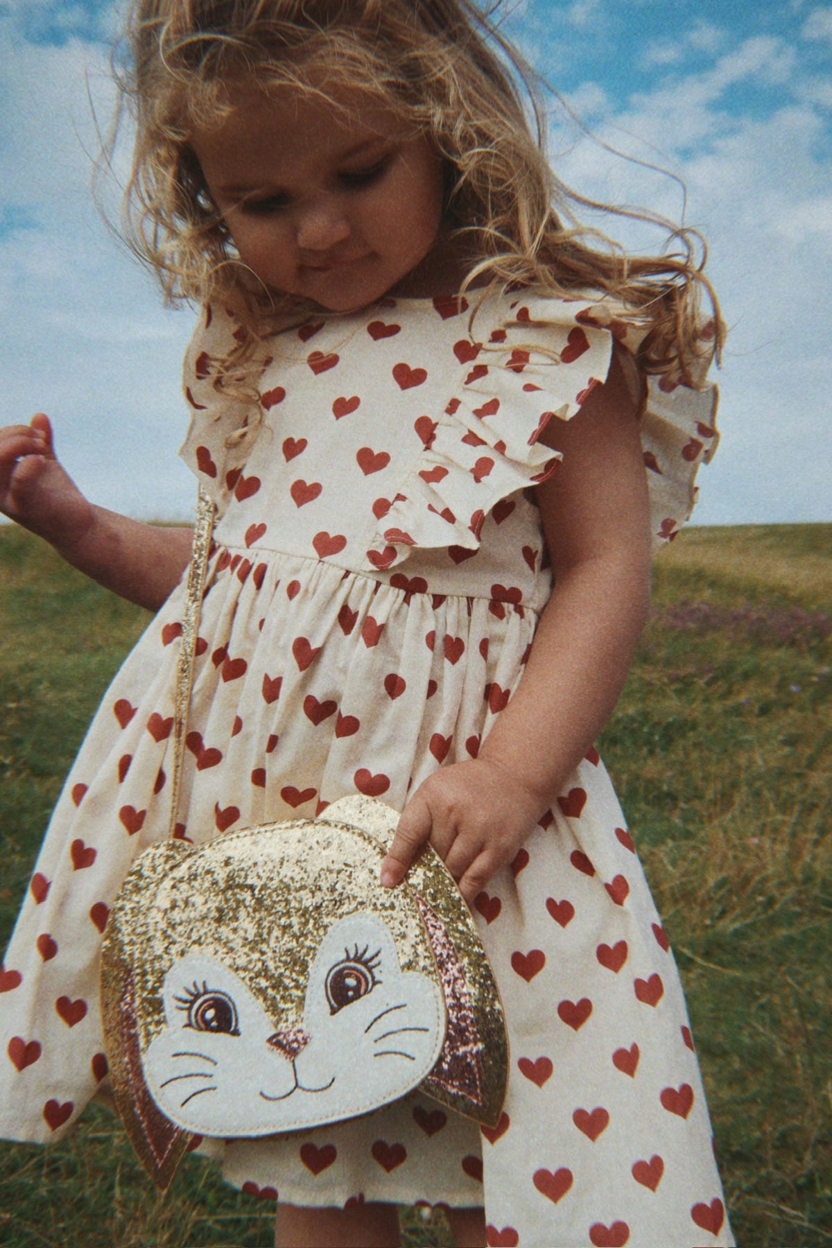 Child in a Konges Sløjd Cianna bow dress in Amour rouge holding a bunny-shaped bag in a field.
