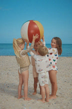Child wearing the Konges Sløjd Ellis swim vest in bon coeur coloré while playing with children and a beach ball on a sandy beach