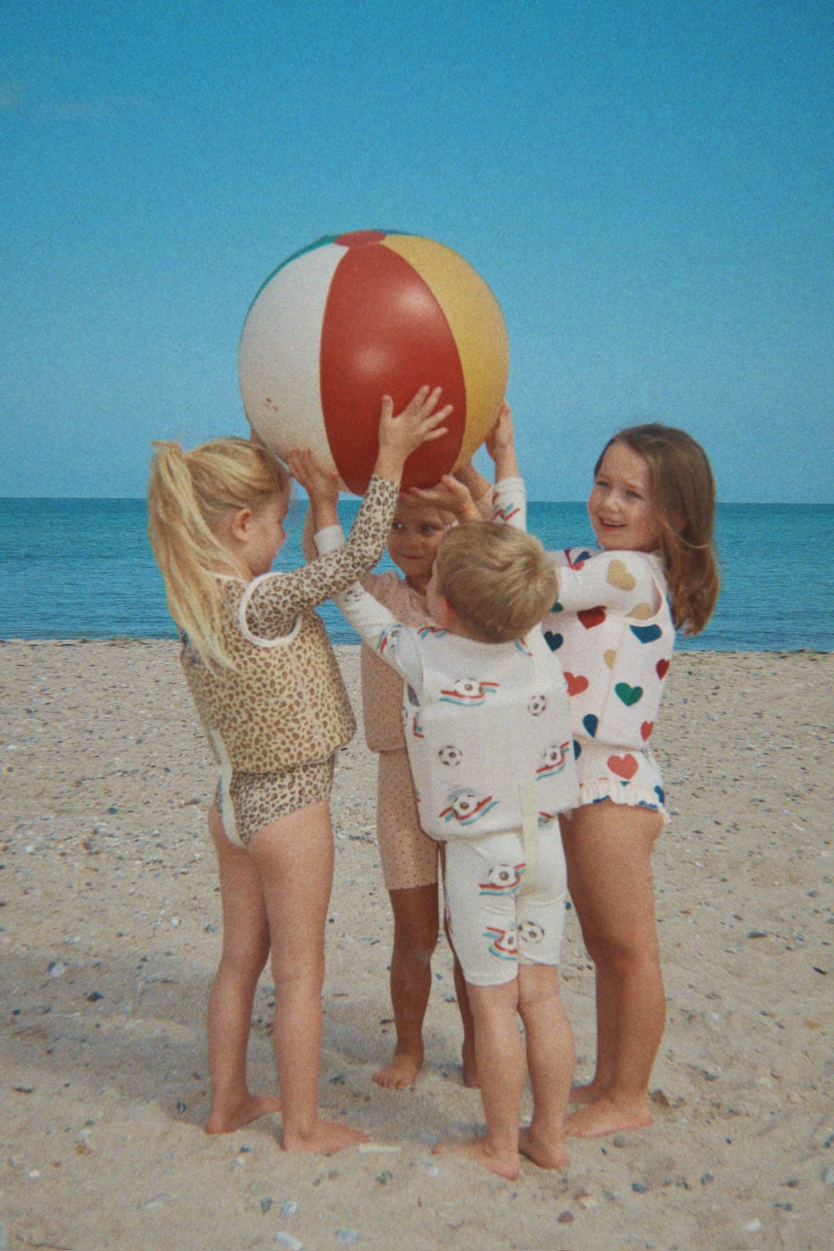 Child wearing the Konges Sløjd Ellis swim vest in bon coeur coloré while playing with children and a beach ball on a sandy beach