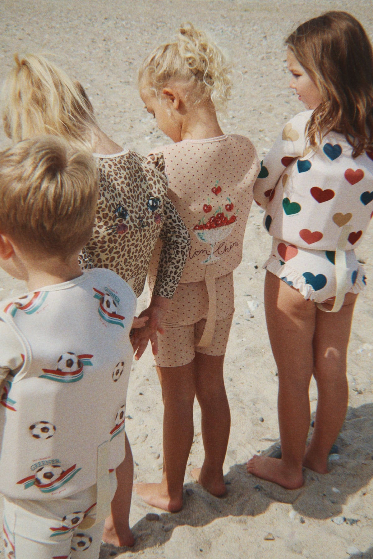 Child wearing a Konges Sløjd Ellis swim vest in bon coeur coloré while standing next to other children on a sandy beach