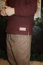 Close-up of a young child wearing the Konges Sløjd Foret Pants in Chocolate Check and a brown sweater.