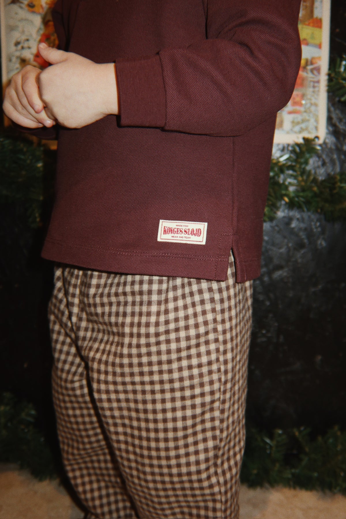 Close-up of a young child wearing the Konges Sløjd Foret Pants in Chocolate Check and a brown sweater.