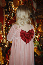 A child seen from behind wearing the Konges Sløjd Gia Bow Dress in Mellow Rose, standing in front of Christmas decoration.