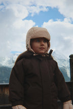 Child wearing the Konges Sløjd Juno hat in Laurel Oak and dark coat with mountains in the background.