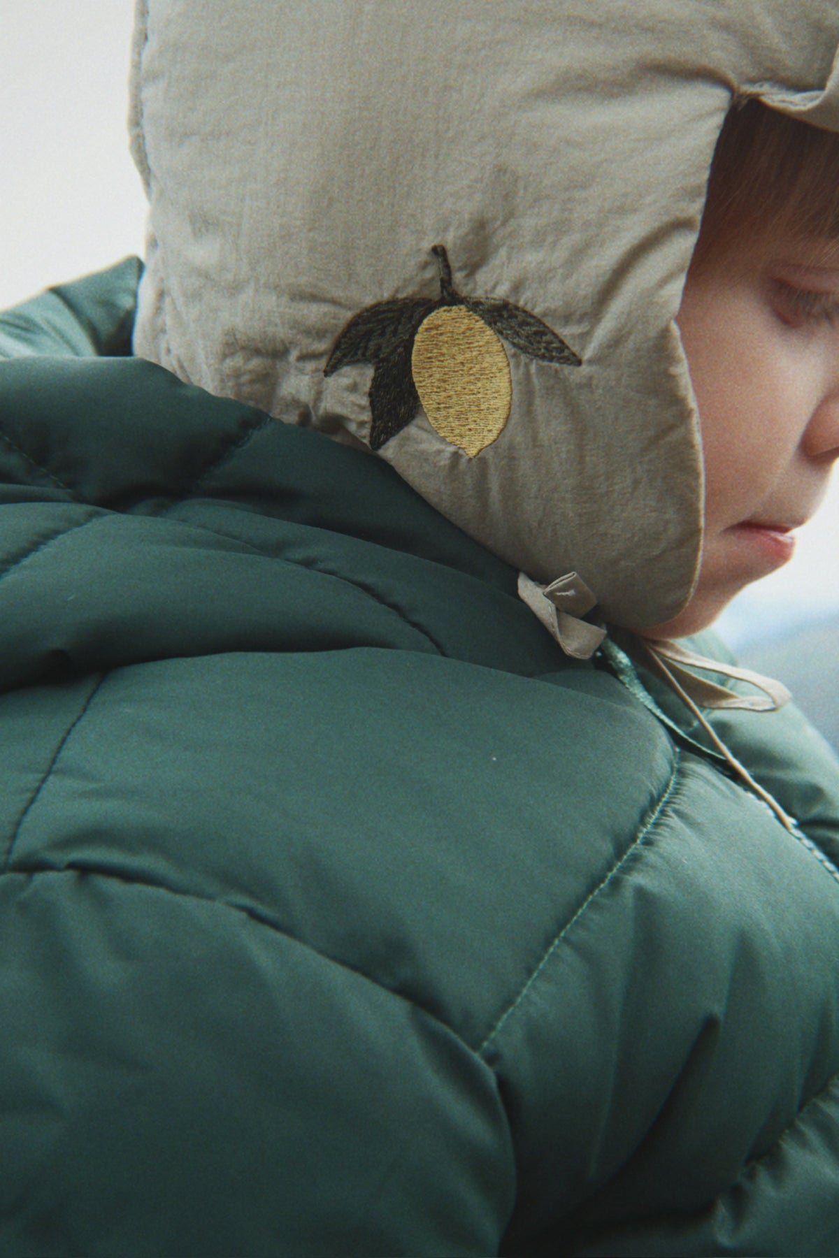 A child wearing the Konges Sløjd Juno hat in Laurel Oak and a green winter jacket.