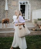 Mushie pacifier case in Natural on a beige tote bag carried by woman outdoors