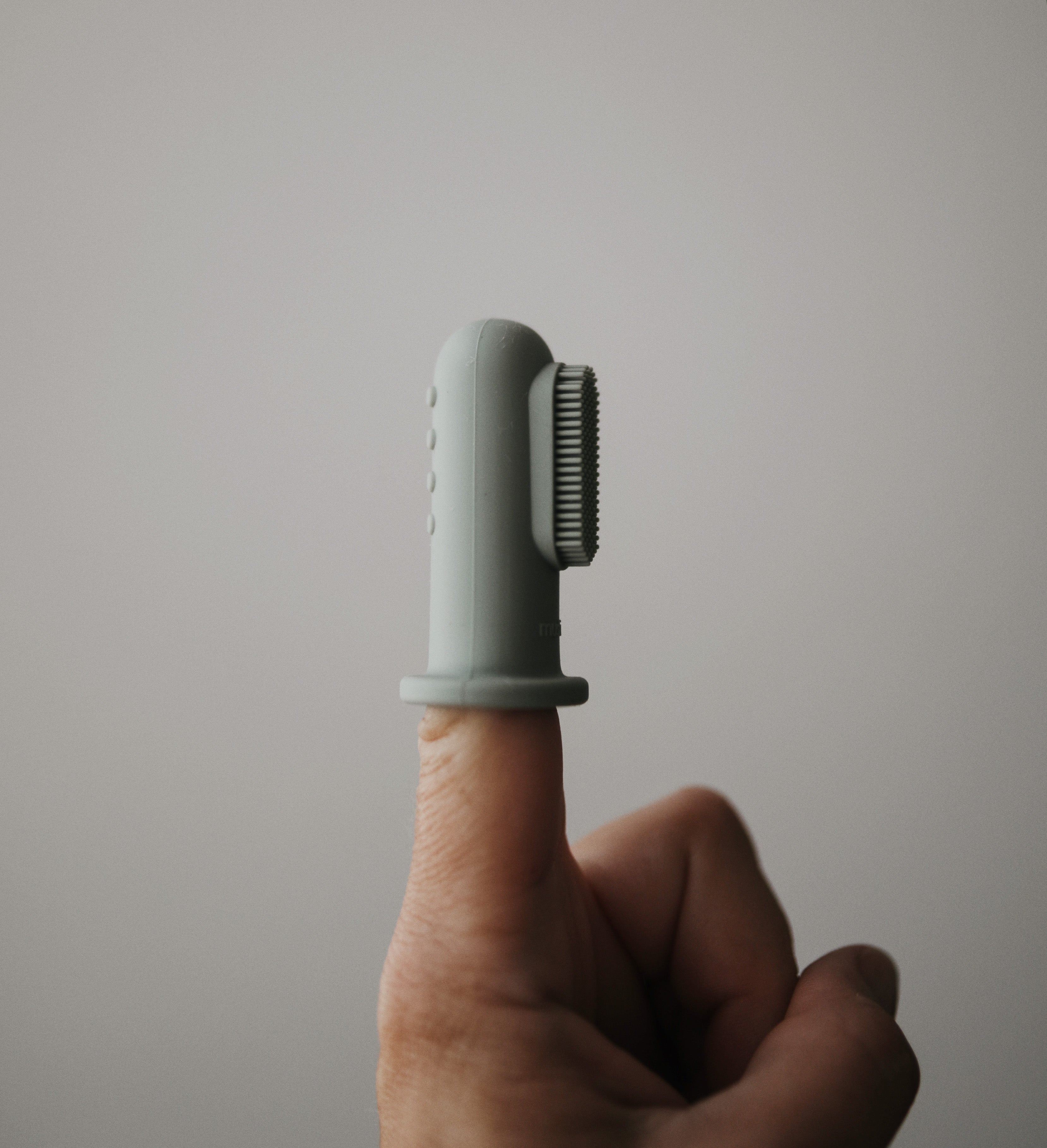 Mushie finger toothbrush in Cambridge blue on a neutral background