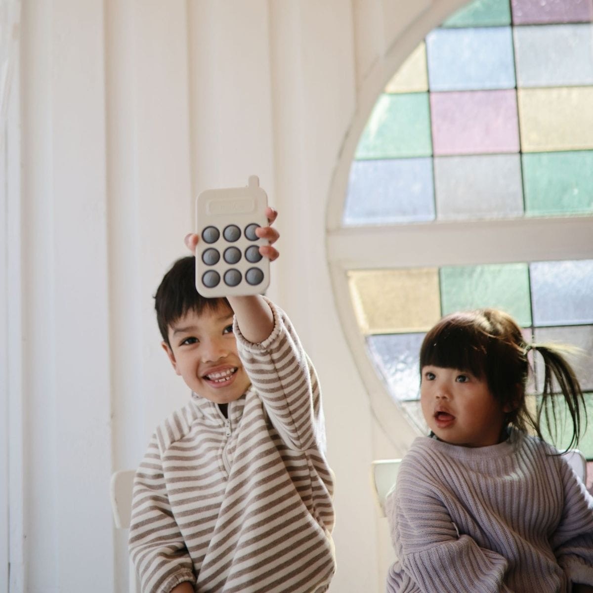 Two children sitting together, one holding the press toy from the Mushie and FRIGG Giftbox Boy