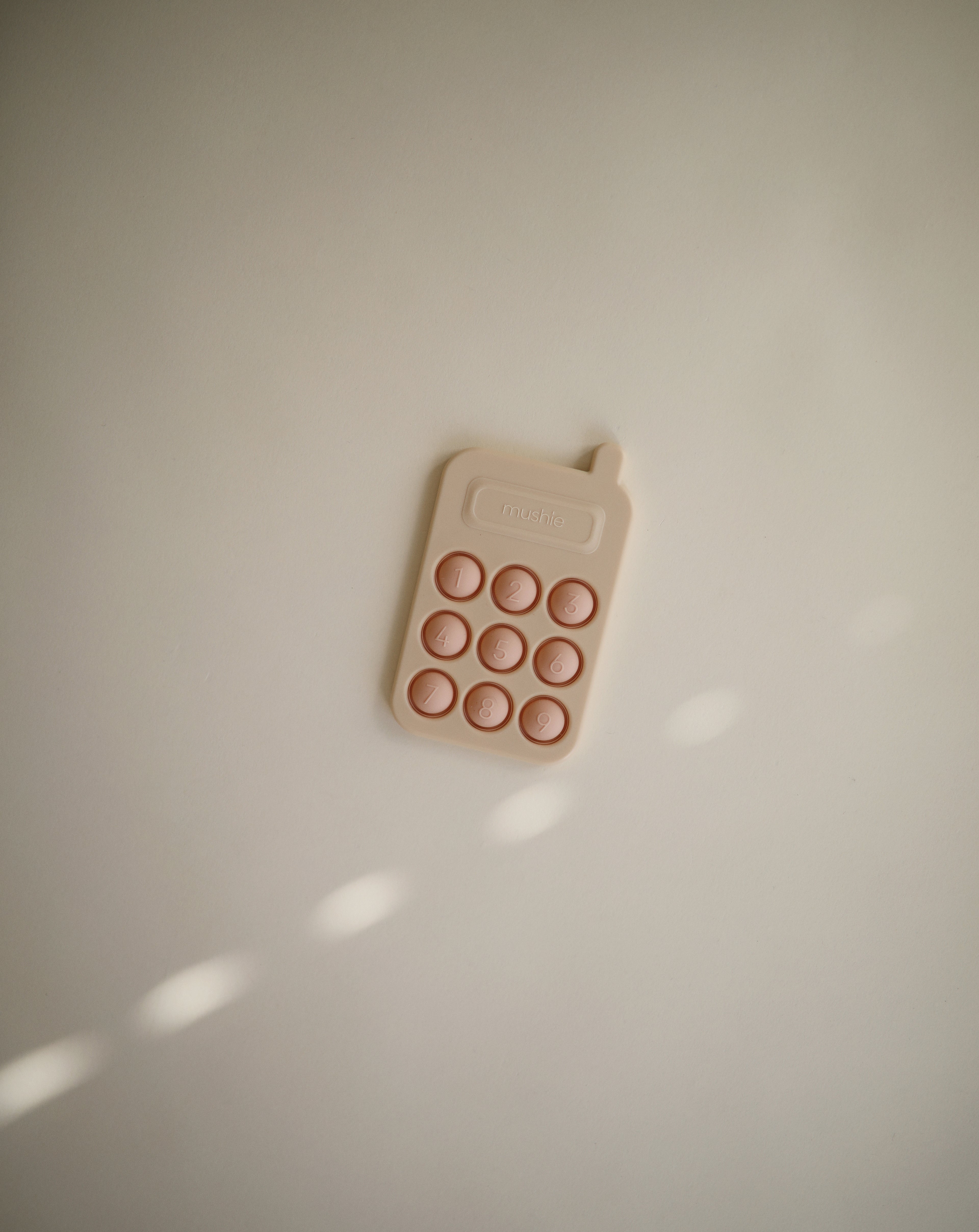 Mushie press toy phone in Blush on a beige background