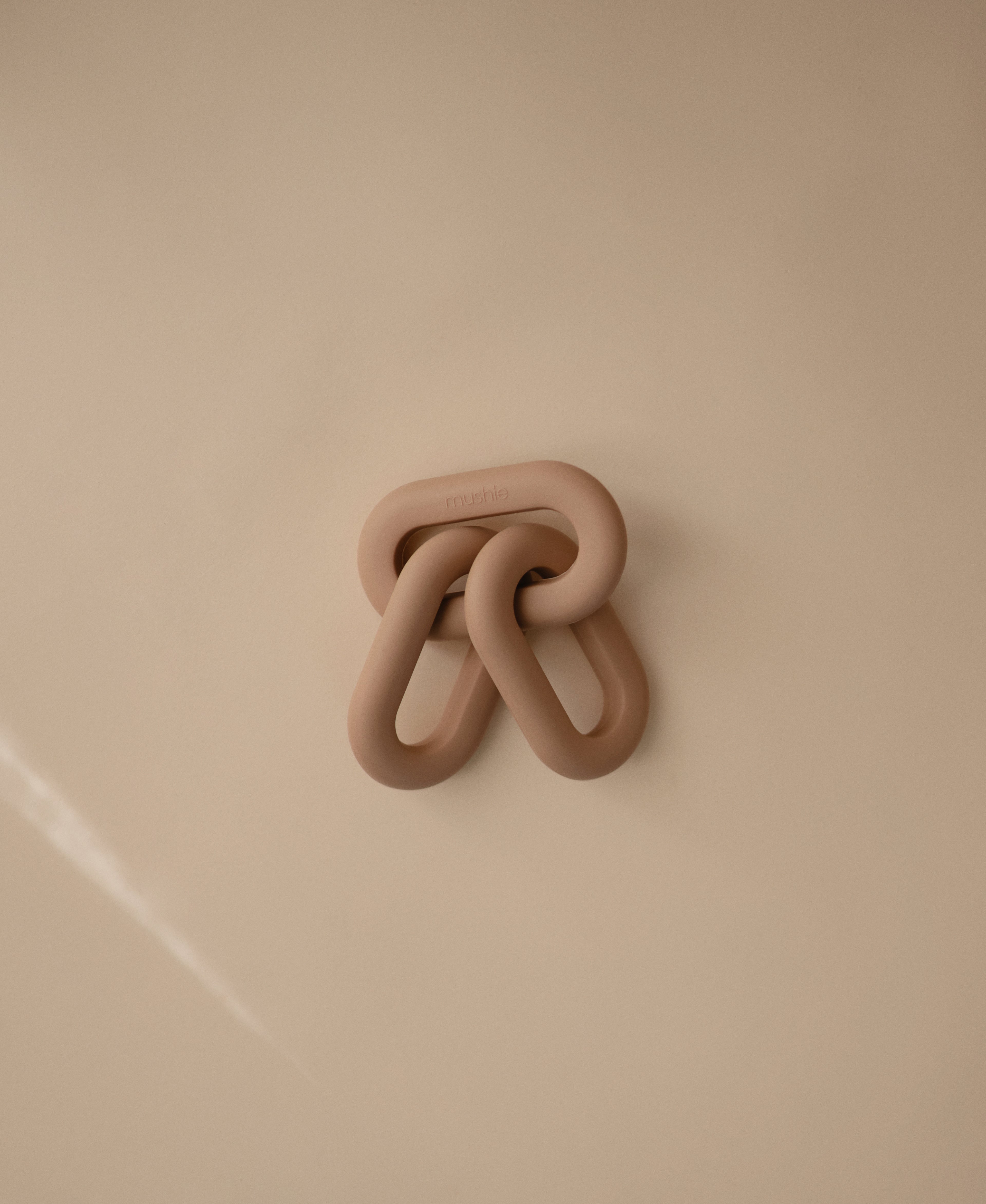 Mushie links teether in Natural on a beige background