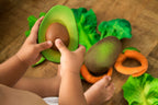 Child playing with a Oli&Carol Arnold the Avocado natural rubber teether and other fruits on a wooden surface