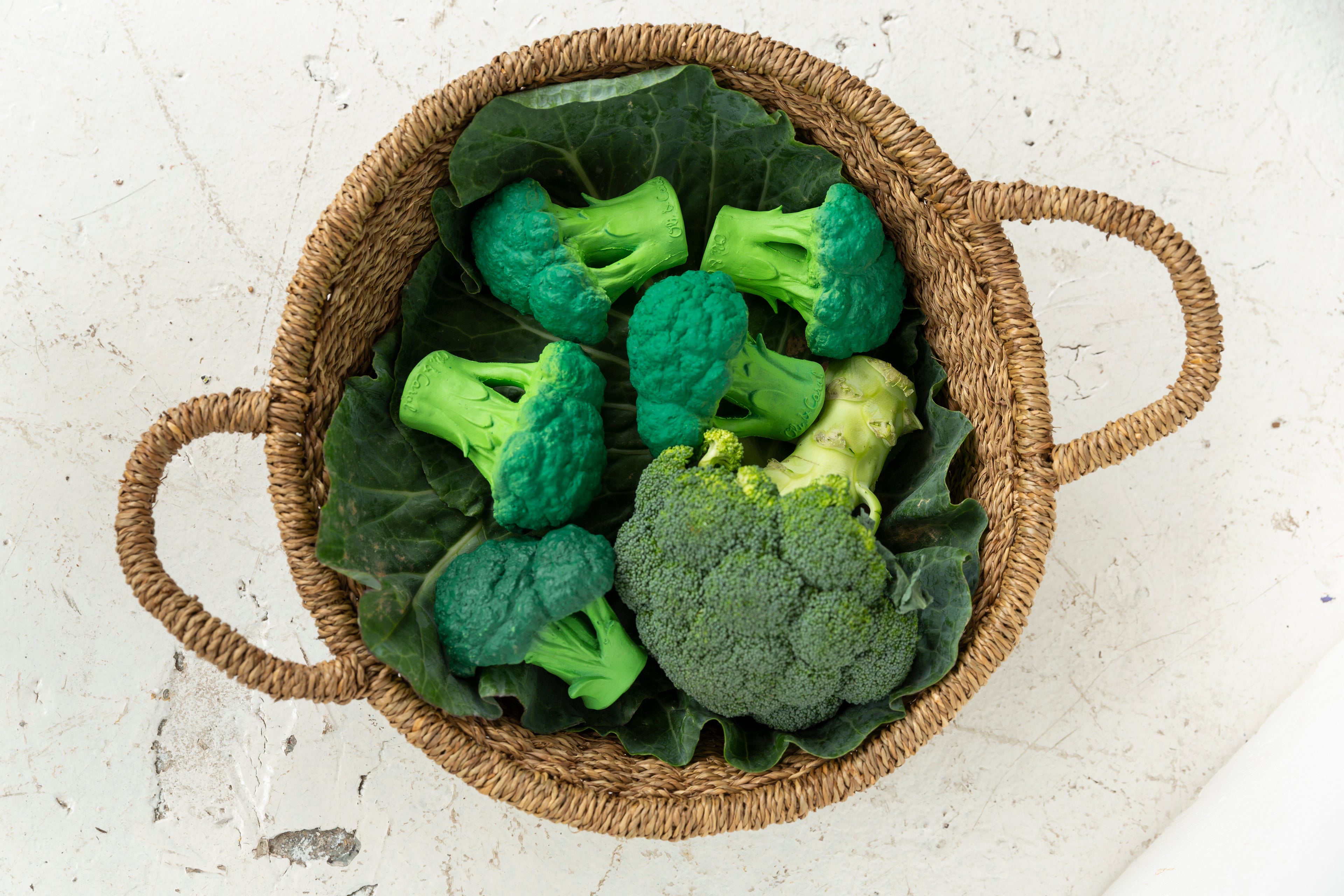 Oli&Carol Brucy the Broccoli natural rubber teether in a woven basket on a light surface