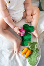 Child playing with a teether, lying next to an Oli&Carol Cathy the Carrot doudou teether in natural rubber