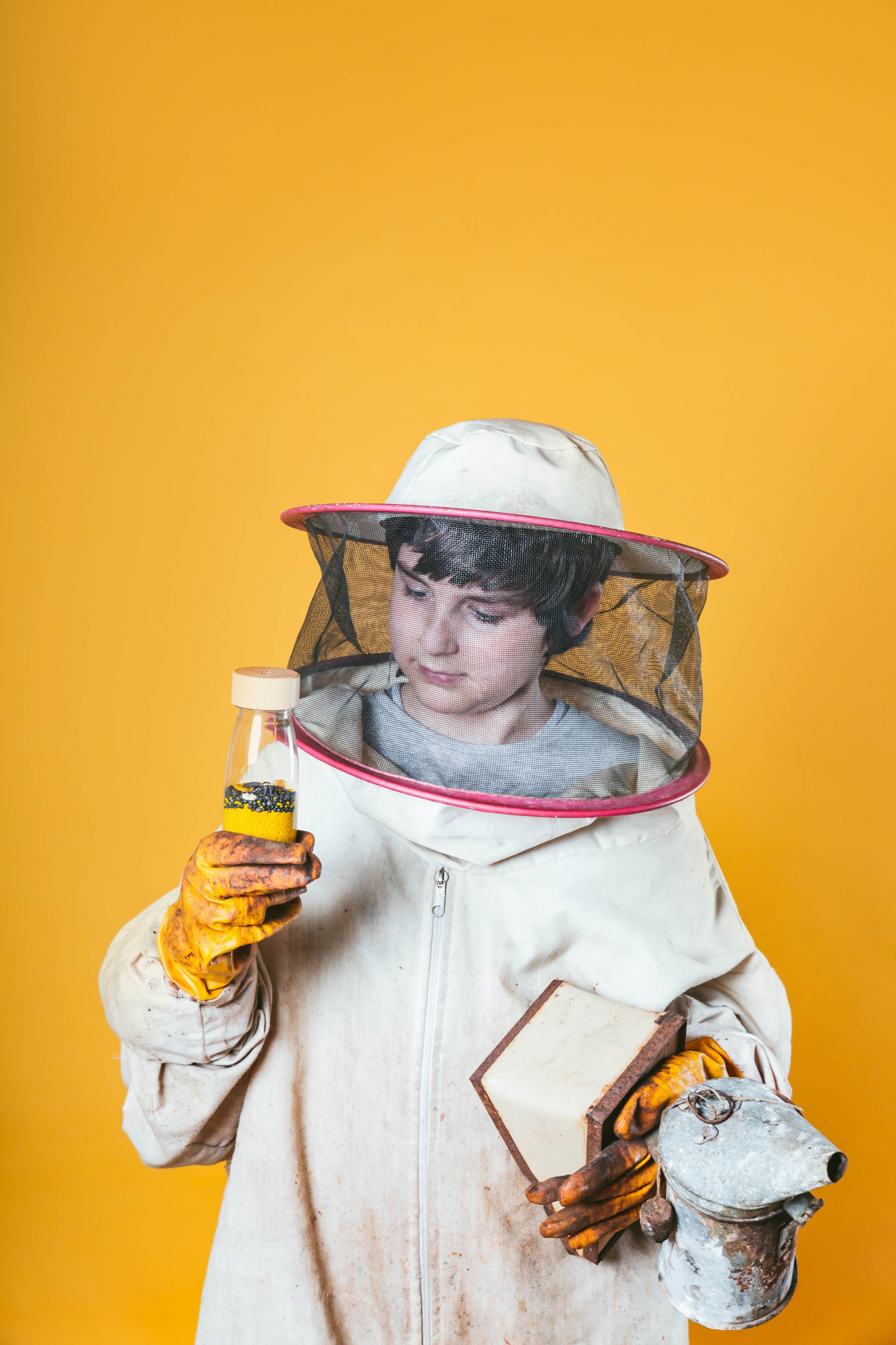 Petit Boum Bees sensory bottle held by a child dressed in a beeholder costume against a yellow background