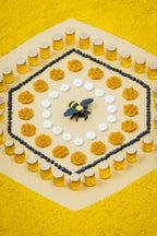Petit Boum Bees sensory bottle lifestyle image in bee theme on a yellow background showing a bee, honeycomb, honey jars and daisies arranged around it