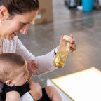 Lifestyle image of a woman holding a baby and the Petit Boum Golden sensory bottle 