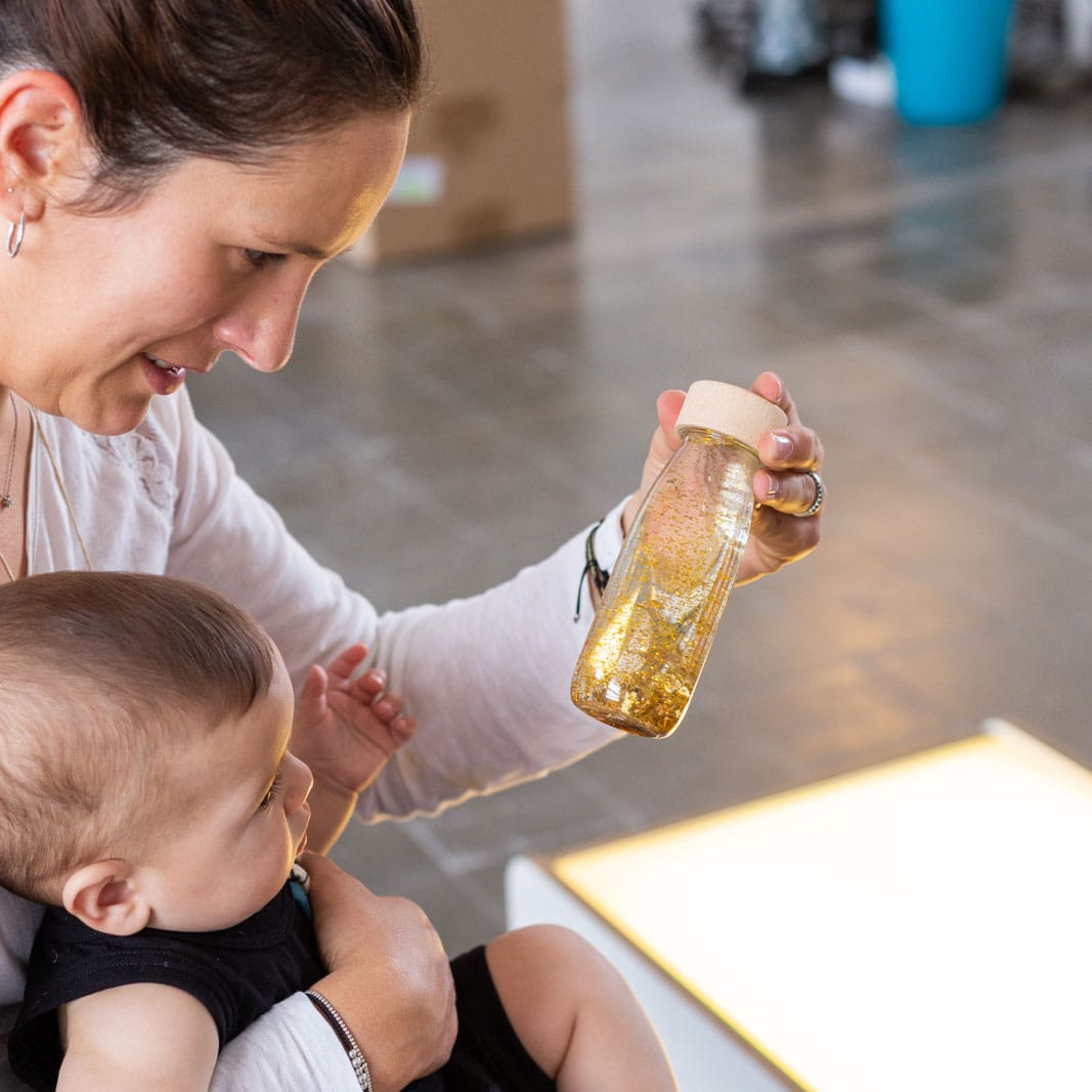 Lifestyle image of a woman holding a baby and the Petit Boum Golden sensory bottle 