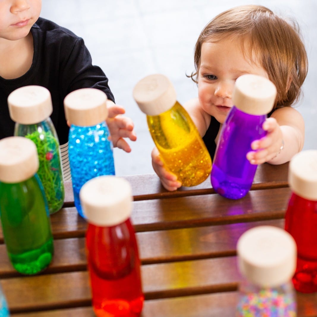 Lifestyle image of two children playing with various Petit Boum bottles, including the Petit Boum Golden sensory bottle