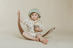 Petit Boum Monkey sensory bottle lifestyle image of a child holding the sensory toy while sitting on a wooden scooter against a neutral beige background