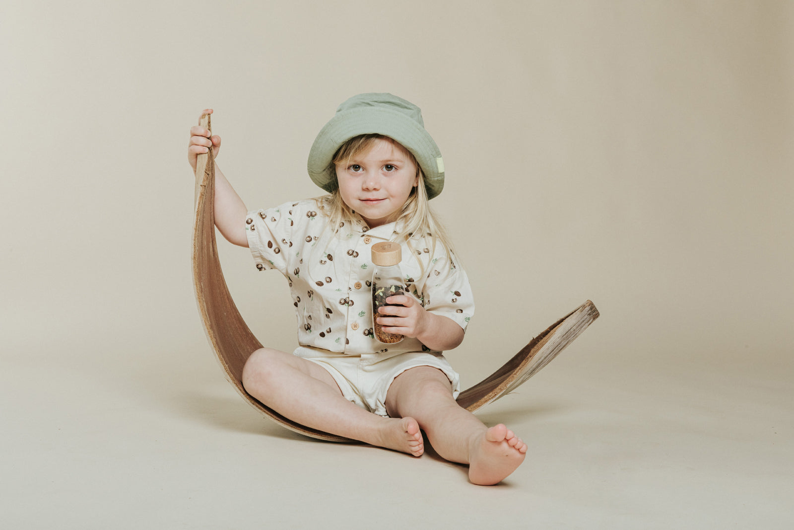 Petit Boum Monkey sensory bottle lifestyle image of a child holding the sensory toy while sitting on a wooden scooter against a neutral beige background