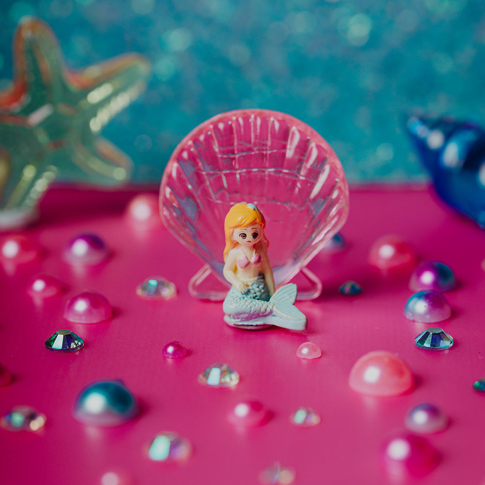 Petit Boum Sea sparkle sensory bottle lifestyle image showing a mermaid with a shell on a pink surface with decorative elements